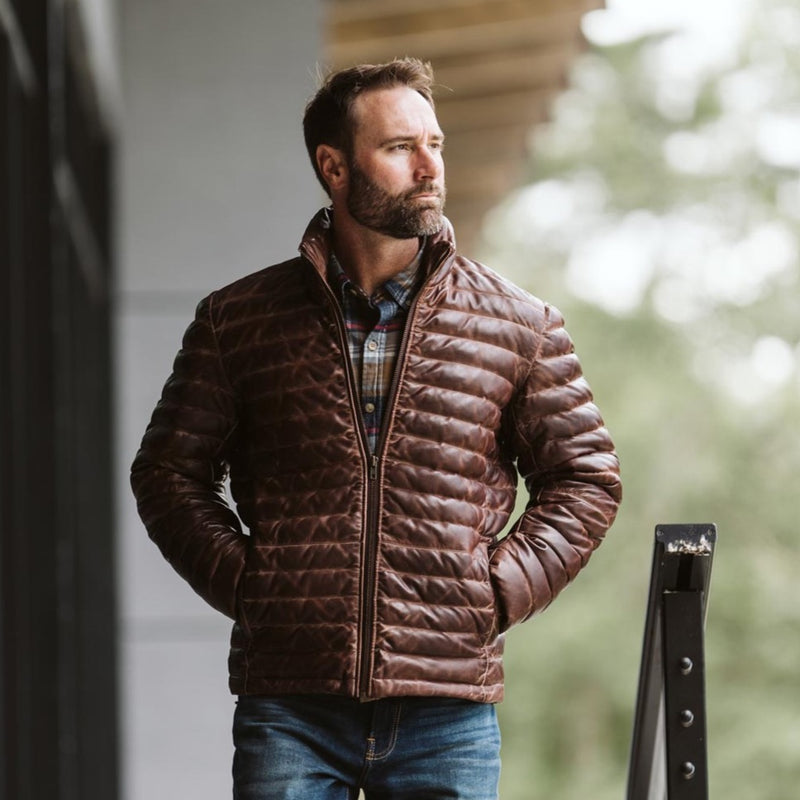 Man wearing the Buffalo Jackson Bridger lambskin leather down jacket outdoors near a mountain cabin